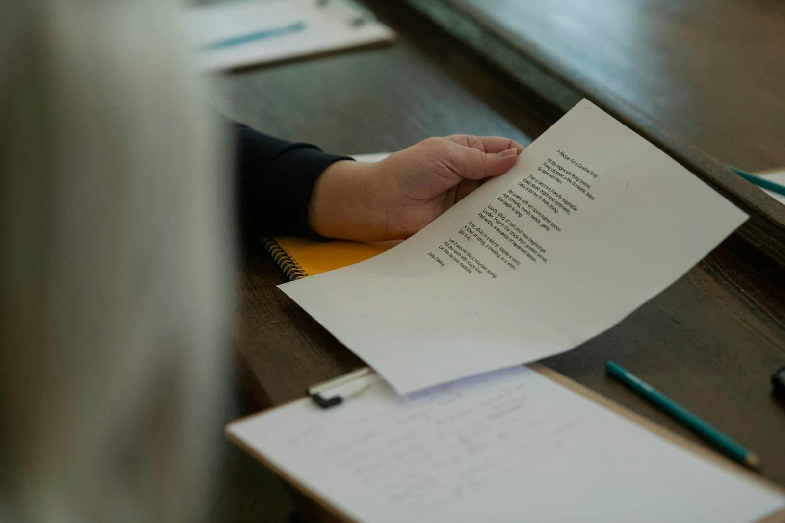 Hand holding a single printed document over a notepad at a wooden desk