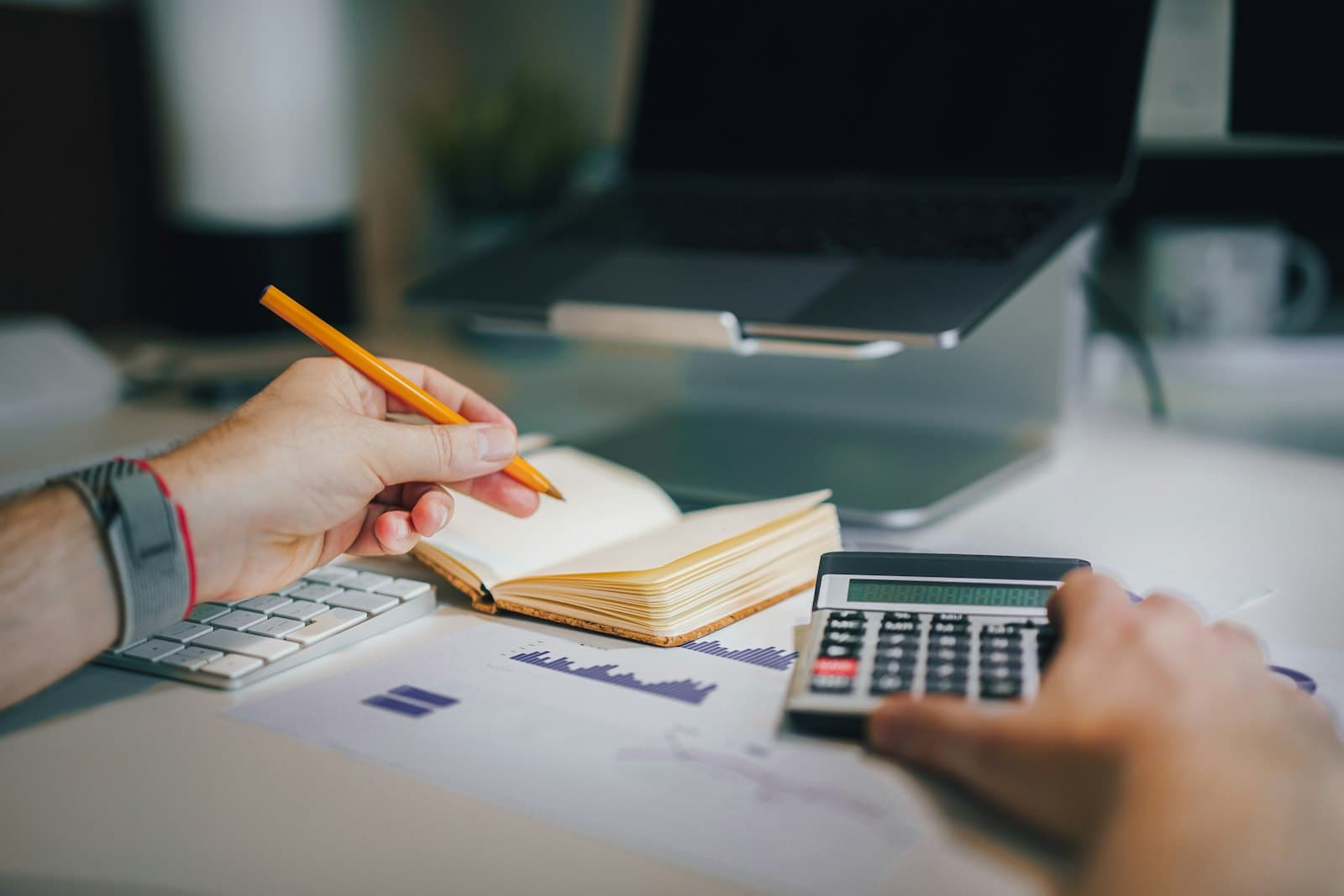 Hands working a calculator and pencil over a printed bar chart report