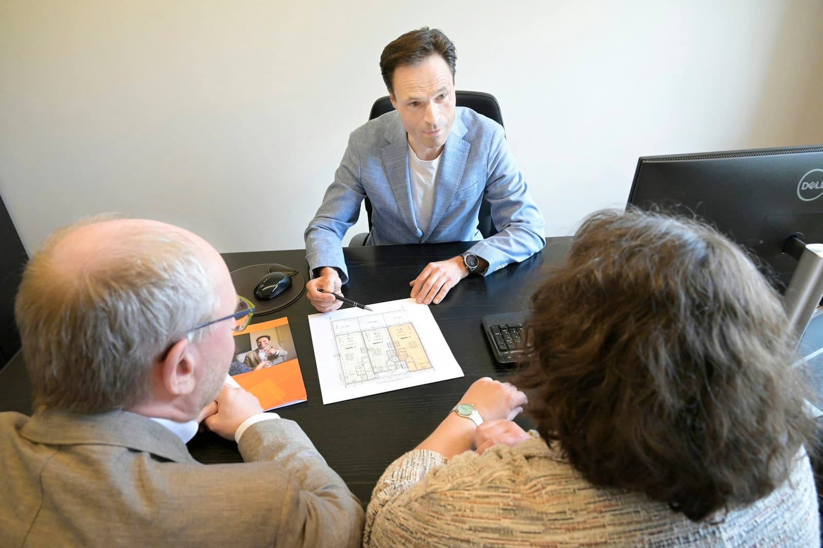 Advisor with a pen walking two seated clients through a printed plan